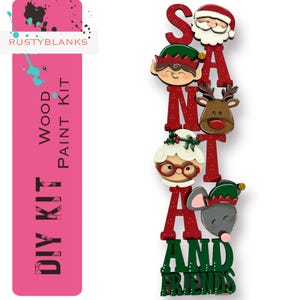 May include: A vertical wooden DIY paint kit featuring the text SANTA AND FRIENDS. The design includes cutouts of Santa Claus, an elf, a reindeer, Mrs. Claus, and a mouse, with red and green lettering. The kit is labeled RUSTYBLANKS WOOD PAINT KIT.