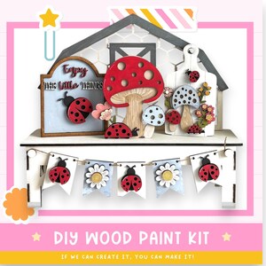 May include: A DIY wood paint kit featuring wooden cutouts of mushrooms, ladybugs, and flowers. The kit includes a sign that reads "Enjoy the little things" and a banner with ladybugs and daisies. The text "DIY WOOD PAINT KIT" is also visible.