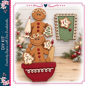 May include: A DIY kit featuring two stacked gingerbread figures in a red mixing bowl with white icing details. One figure holds a piping bag and a tree-shaped cookie. A green rectangular door-shaped piece with a star cookie is also included.