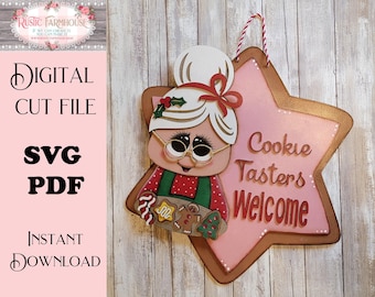 May include: A star-shaped wooden wall hanging featuring a cartoon illustration of an elderly person with white hair in a bun, wearing glasses and a red polka-dot shirt, holding a tray of cookies. The text reads Cookie Tasters Welcome.