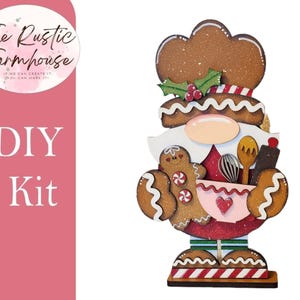 May include: A DIY kit featuring a wooden gnome cutout shaped like a baker with a brown gingerbread-textured hat, a white beard, and a pink mixing bowl. The gnome holds a small gingerbread cookie, a whisk, a wooden spoon, and a rolling pin.