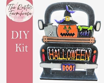 Puede incluir: Un kit de manualidades de Halloween con forma de camión negro que incluye una calabaza con sombrero de bruja, una botella de veneno gris, un caldero verde con el texto eek! y una matrícula que dice BOO!. El portón trasero muestra HALLOWEEN.
