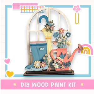 May include: A DIY wood paint kit featuring a wooden window frame with a blue umbrella, boots, and a watering can. The scene is decorated with colorful flowers and a rainbow, perfect for a creative project.