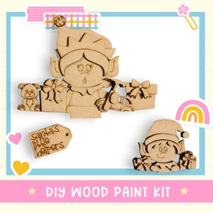 May include: A DIY wood paint kit featuring wooden elf figures holding gifts and a toy car. The kit includes a teddy bear, gift boxes, and a tag that reads "Santa's Little Helpers". The design is surrounded by decorative elements.