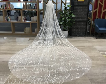 May include: A white bridal veil with a delicate floral pattern and sparkling embellishments. The veil is long and flowing, with a soft tulle fabric.