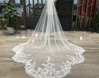 May include: A white bridal veil with a delicate floral lace trim. The veil is made of soft tulle and is long enough to flow behind the bride as she walks down the aisle.