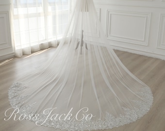 May include: A long, white tulle wedding veil with a beaded edge. The veil is draped over a mannequin and is displayed against a white background.