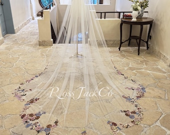 May include: A white tulle wedding veil with a floral embroidery design in shades of pink, blue, and brown. The veil is displayed on a mannequin in a room with a tiled floor.