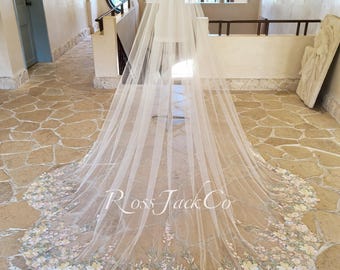 May include: A long, sheer white wedding veil with a floral embroidered border in pastel colors. The veil is displayed on a mannequin in a well-lit room. The text "Ross Jack Co" is visible on the veil.
