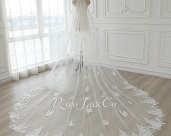 May include: A white bridal veil with a delicate lace trim and floral embroidery. The veil is long and flowing, with a cathedral length. The veil is displayed on a mannequin in a white room.