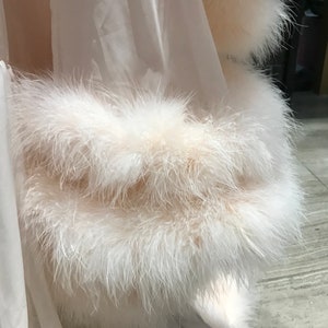 Puede incluir: Una bata blanca transparente con un ribete de plumas blancas y esponjosas alrededor de los bordes.