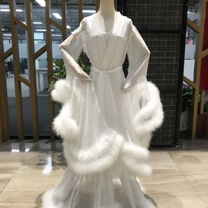 May include: A white sheer robe with long sleeves and a fluffy white trim around the edges. The robe has a sash tie at the waist.