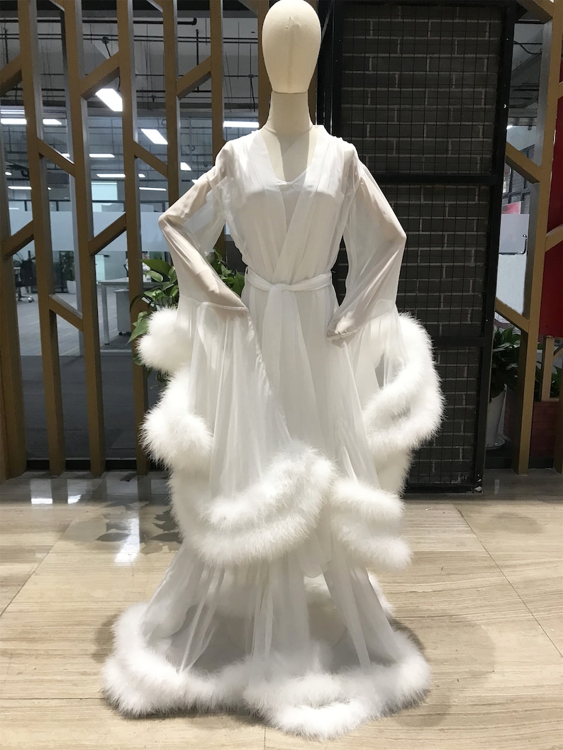 May include: A white sheer robe with long sleeves and a fluffy white trim around the edges. The robe has a sash tie at the waist.