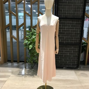Puede incluir: Un vestido de sat&eacute;n rosa claro con tirantes finos. El vestido est&aacute; en un maniqu&iacute; y tiene un escote en V.