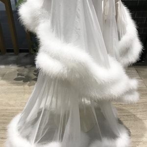 May include: White sheer robe with a fluffy white feather trim around the edges. The robe is made of a lightweight, flowing fabric.