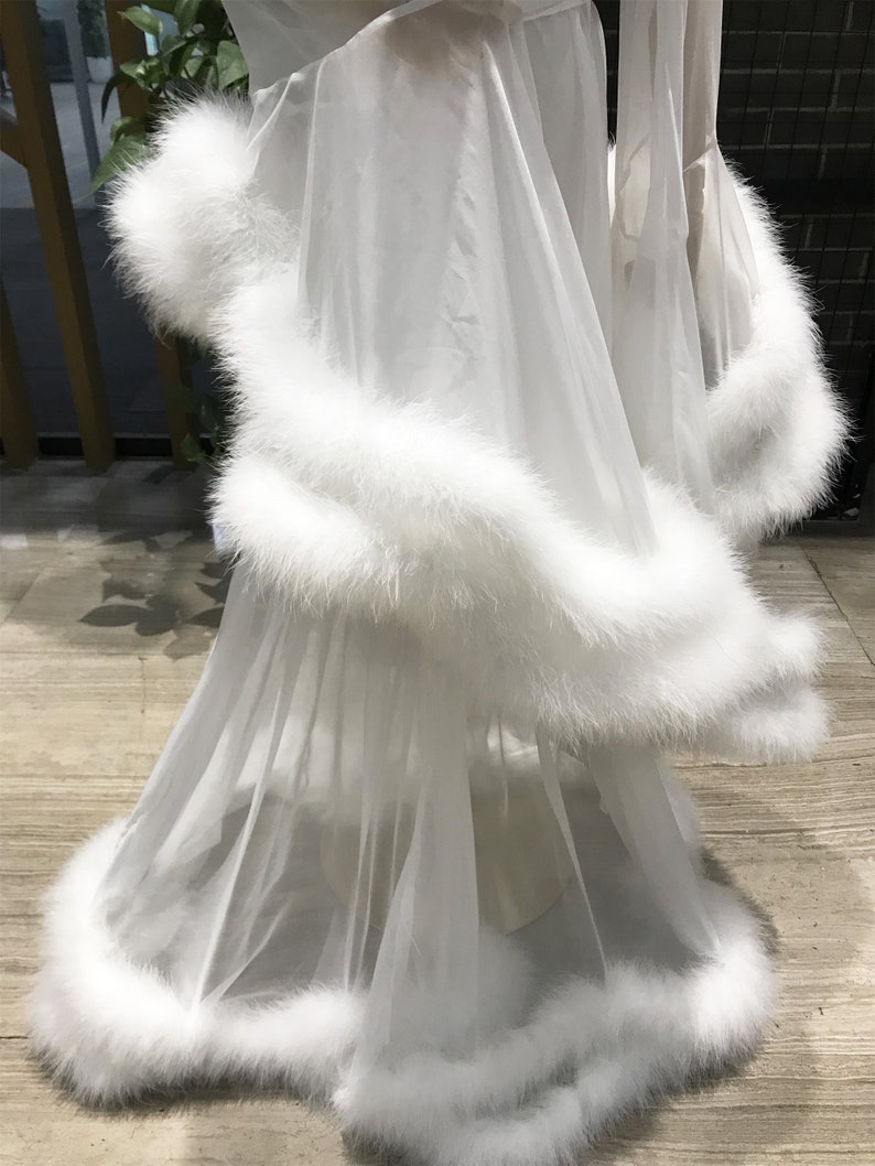 May include: White sheer robe with a fluffy white feather trim around the edges. The robe is made of a lightweight, flowing fabric.