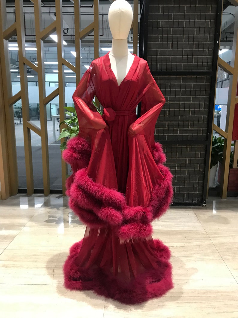 Puede incluir: Una larga bata roja con cuello en V y mangas largas. La bata tiene una faja en la cintura y est&aacute; adornada con una gruesa banda de plumas burdeos.