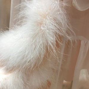 Puede incluir: Una prenda de vestir de tela blanca transparente con un ribete de plumas blancas. El ribete de plumas es de capas y esponjoso.