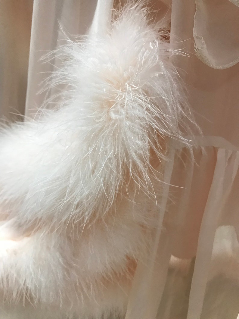 Puede incluir: Una prenda de vestir de tela blanca transparente con un ribete de plumas blancas. El ribete de plumas es de capas y esponjoso.