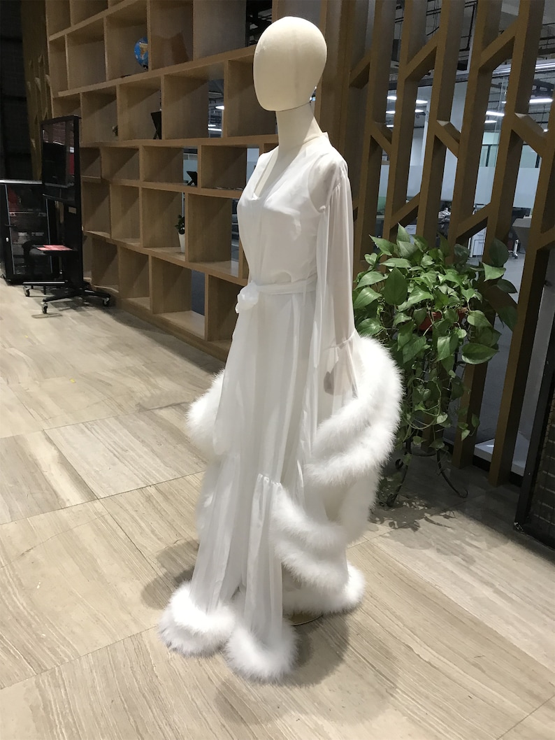 May include: A white sheer robe with a long sleeve and a white feather trim. The robe has a sash at the waist and a V-neckline.
