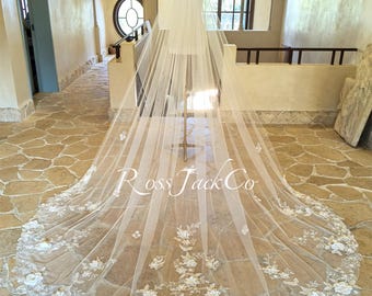 May include: A long, white bridal veil with delicate floral lace trim. The veil is displayed on a mannequin in a room with a stone floor and arched doorways. The text "Ross Jack Co" is visible on the veil.