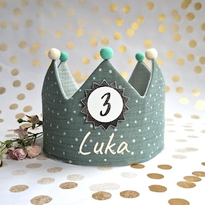 Könnte beinhalten: Eine teal-farbene Stoffkrone mit weißen Punkten, mit einem silbernen Stern mit der Zahl 3 und dem Namen "Luka". Die Krone hat drei Pompons oben und ist für eine Kindergeburtstagsfeier gedacht.