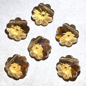May include: Six gold-toned flower-shaped glass beads with a hole through the center for stringing.