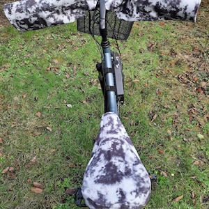 Peut inclure: Un vélo noir avec une housse de selle et des couvre-guidons à motifs tie-dye blancs et noirs. Le vélo a un panier noir à l'avant.
