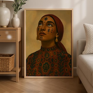 May include: A framed portrait of a person with dark skin, wearing a red headscarf and a patterned red and green top. The person has decorative markings on their face and is looking upwards. Gold earrings are visible.