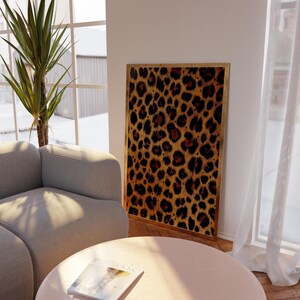 May include: A framed print of a leopard print pattern in shades of brown, orange, and black. The print is hanging on a white wall in a living room setting.