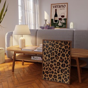 May include: A framed print of a leopard print pattern. The print is in shades of brown, black, and tan. The print is hanging on a wall in a living room setting.