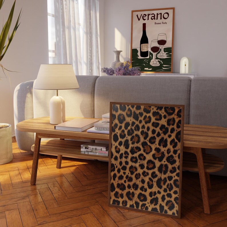 May include: A framed print of a leopard print pattern. The print is in shades of brown, black, and tan. The print is hanging on a wall in a living room setting.
