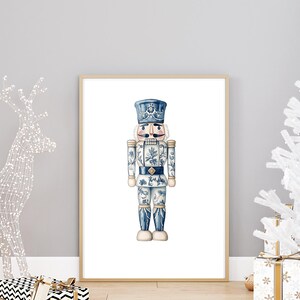 May include: A blue and white porcelain nutcracker with a blue hat and a white face. The nutcracker is standing on a white background.