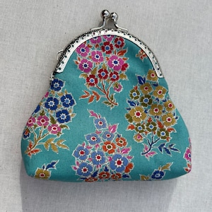 May include: A small, teal blue coin purse with a silver clasp. The purse is decorated with a floral pattern in shades of pink, blue, yellow, and green.