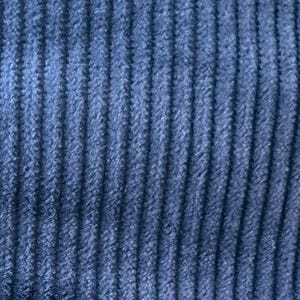 Op de afbeelding: Close-up van een blauwe corduroy stof met een verticale ribbelstructuur.