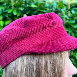 May include: A burgundy corduroy newsboy cap with a slightly curved brim.