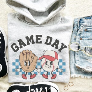 May include: A gray hoodie with the text "GAME DAY" printed on the front. The hoodie features a cartoon baseball and a baseball glove with faces.