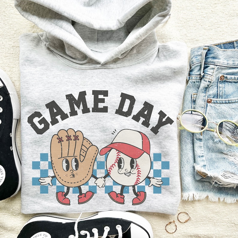 May include: A gray hoodie with the text "GAME DAY" printed on the front. The hoodie features a cartoon baseball and a baseball glove with faces.
