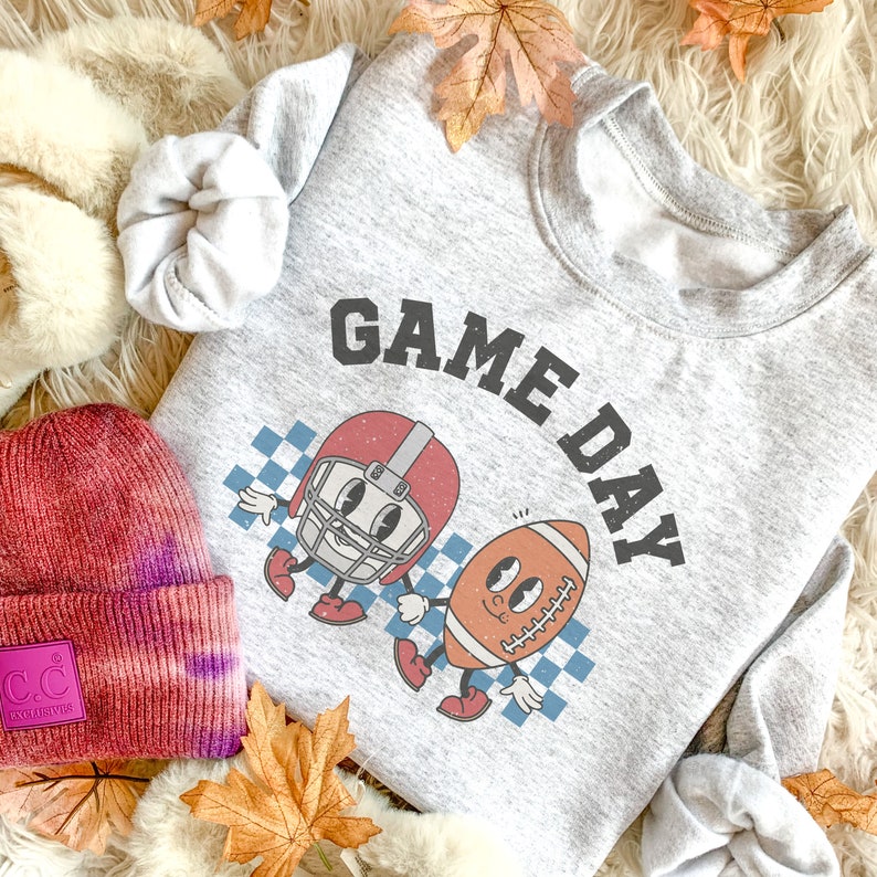 May include: A gray sweatshirt with the text "GAME DAY" in large, black letters. The sweatshirt features a cartoon football helmet and football with faces.