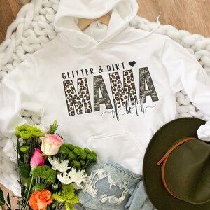 K&ouml;nnte beinhalten: Wei&szlig;er Kapuzenpullover mit dem Text "Glitter & Dirt Mama of both" in schwarzem und braunem Leopardenmuster und Tarnmuster.