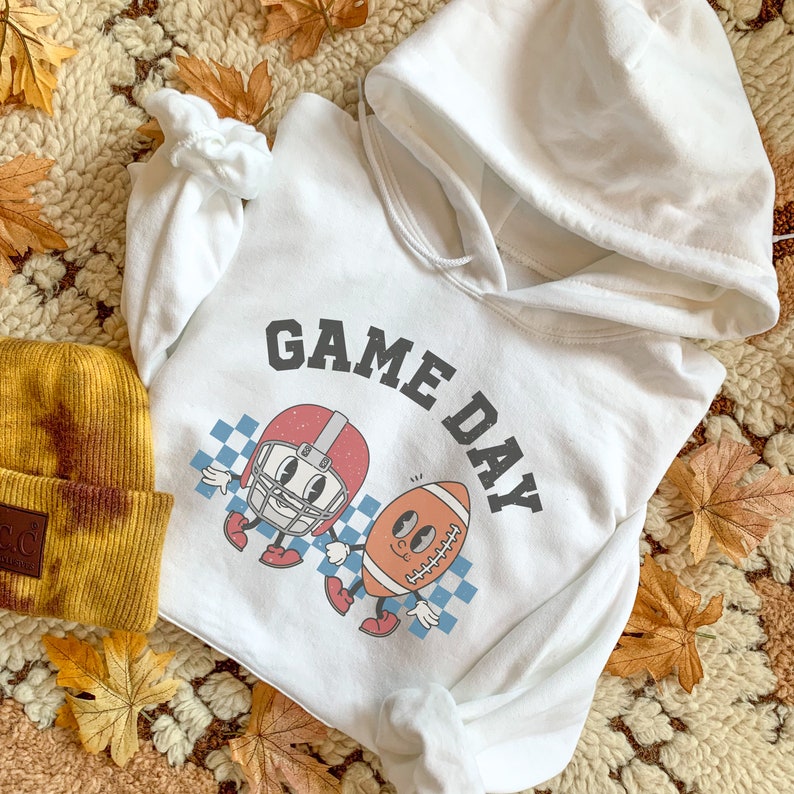 May include: White hooded sweatshirt with a graphic of a football and a football helmet with the text "GAME DAY" printed on the front.
