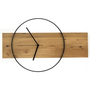 Może przedstawiać: Nowoczesny zegar ścienny z czarną metalową ramką i drewnianą podstawą. Wskazówki zegara są czarne, a tarcza to prosty okrąg.