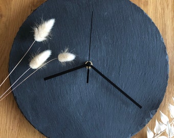 Può includere: Un orologio in ardesia nera con lancette nere e un centro dorato. L'orologio è su una superficie di legno.