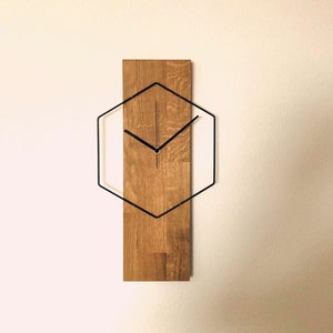 Könnte beinhalten: Eine Wanduhr aus Holz mit einem schwarzen sechseckigen Rahmen und schwarzen Zeigern. Das Zifferblatt der Uhr ist aus Holz mit natürlicher Maserung.
