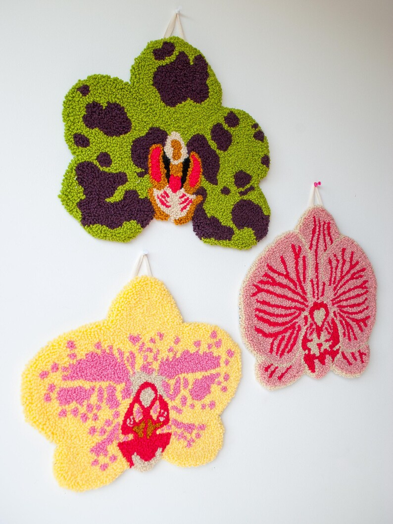 Pode incluir: Tr&ecirc;s tape&ccedil;arias de parede de orqu&iacute;deas tufadas e coloridas. A superior &eacute; verde com manchas roxas escuras. A do meio &eacute; amarela com detalhes em rosa, e a inferior &eacute; rosa com detalhes em vermelho. Cada uma tem uma argola para pendurar.