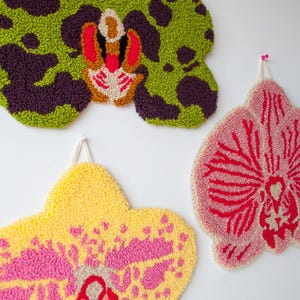 Pode incluir: Tr&ecirc;s penduradas de parede de orqu&iacute;deas texturizadas e coloridas. A superior &eacute; verde com manchas roxas escuras e um centro vermelho e bege. A inferior esquerda &eacute; amarela com detalhes rosa, e a inferior direita &eacute; rosa com detalhes vermelhos.