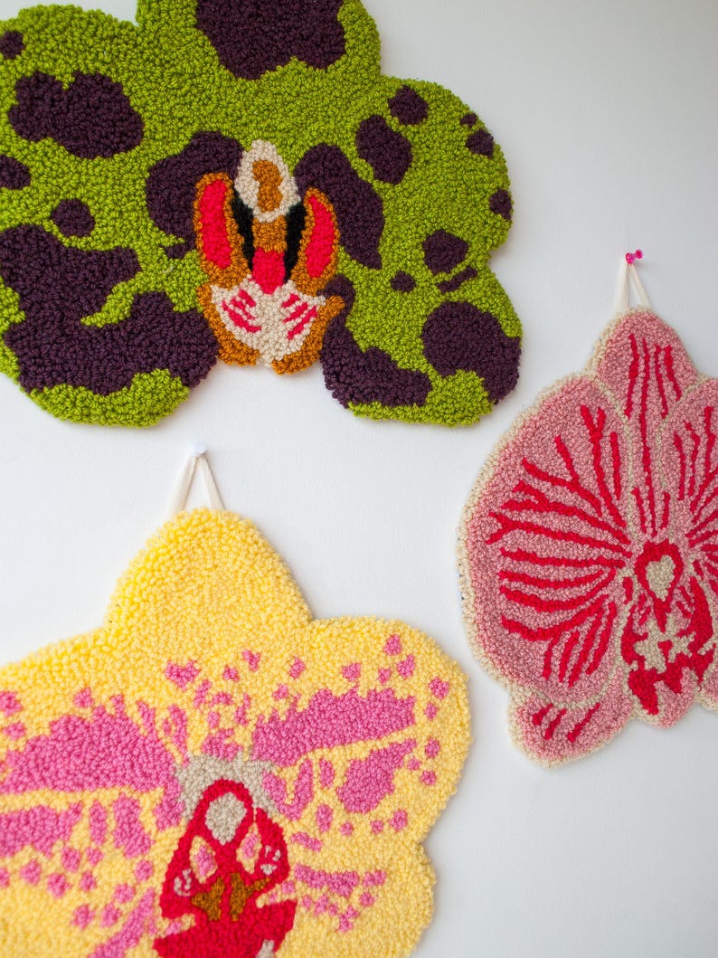 Pode incluir: Tr&ecirc;s penduradas de parede de orqu&iacute;deas texturizadas e coloridas. A superior &eacute; verde com manchas roxas escuras e um centro vermelho e bege. A inferior esquerda &eacute; amarela com detalhes rosa, e a inferior direita &eacute; rosa com detalhes vermelhos.