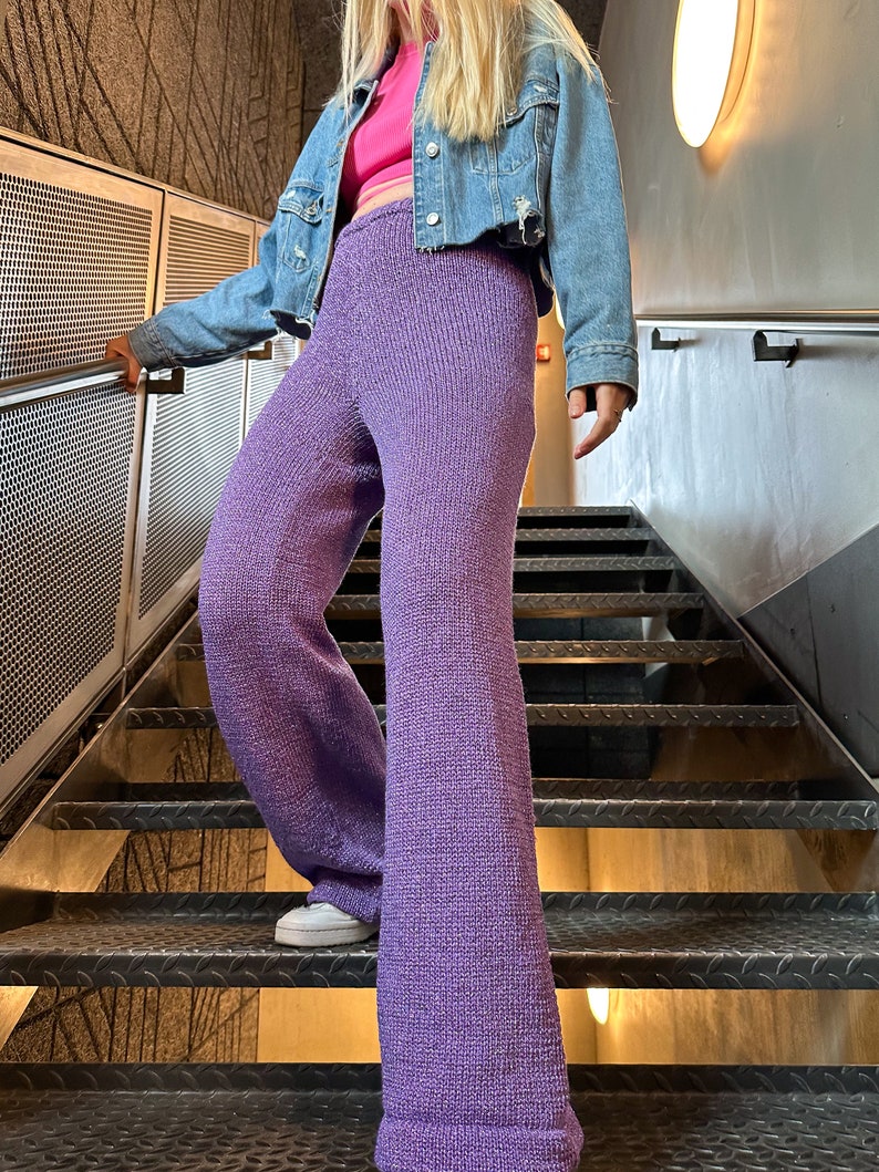 May include: Purple knitted wide-leg trousers with a slightly flared hem. The trousers are worn with a denim jacket and a pink crop top.