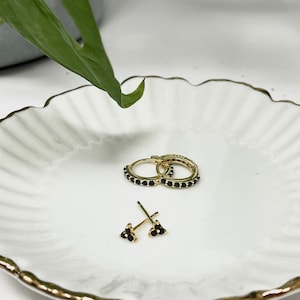 May include: A pair of gold hoop earrings with black stones and a pair of gold stud earrings with black stones on a white plate.