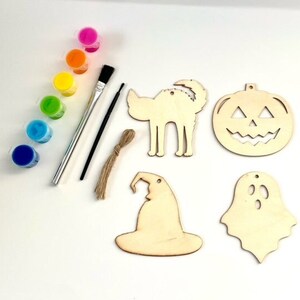 May include: A Halloween craft kit with six wooden ornaments, a paintbrush, and six small bottles of paint. The ornaments are shaped like a pumpkin, a ghost, a witch's hat, a cat, and two bats. The paint is in rainbow colors.